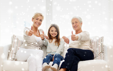 family, happiness, generation and people concept - smiling mother, daughter and grandmother sitting on couch and showing thumbs up gesture at homeの写真素材