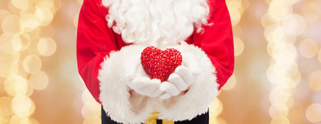 christmas, holidays, love, charity and people concept - close up of santa claus with heart shape decoration over beige lights backgroundの写真素材