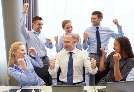 business, people, technology, gesture and teamwork concept - smiling business team raising hands and celebrating victory in officeの写真素材
