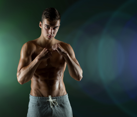 sport, competition, strength and people concept - young man in fighting or boxing position over darkの写真素材