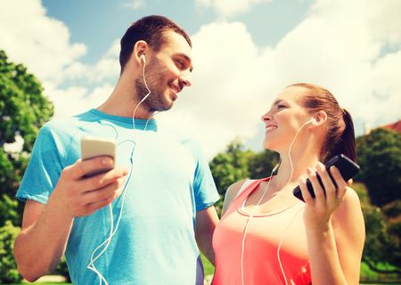 fitness, sport, training, technology and lifestyle concept - two smiling people with smartphones and earphones outdoorsの写真素材