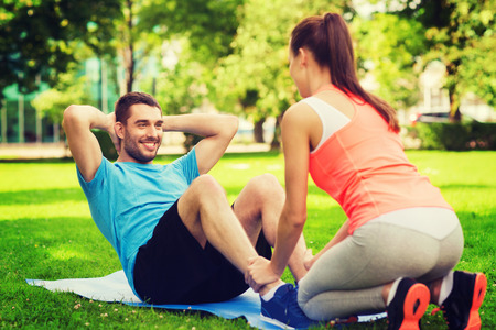 fitness, sport, training, teamwork and lifestyle concept - smiling man with personal trainer doing exercises on mat outdoorsの写真素材