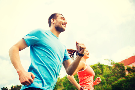 fitness, sport, friendship and lifestyle concept - smiling couple running outdoors