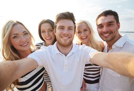 summer, sea, tourism, technology and people concept - group of smiling friends with camera on beach photographing and taking selfieの写真素材