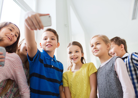 education, elementary school, drinks, children and people concept - group of school kids taking selfie with smartphone in corridorの写真素材