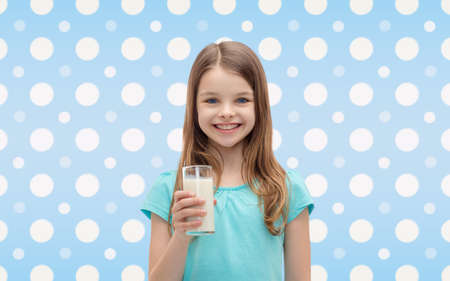 healthcare, food, drinks, childhood and people concept - smiling little girl with glass of milk over blue white polka dots pattern の写真素材