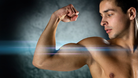 sport, bodybuilding, strength and people concept - close up of young man flexing and showing biceps over darkの写真素材
