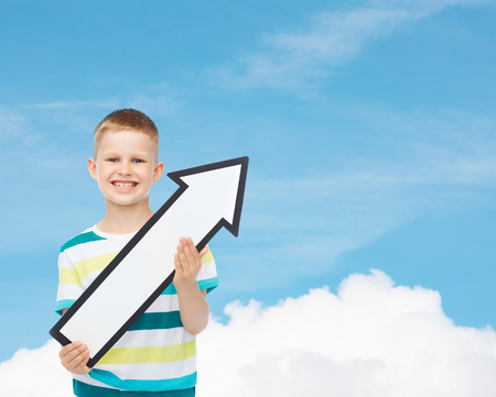 advertising, direction and childhood concept - smiling little boy with white blank arrow pointing up over blue skyの写真素材