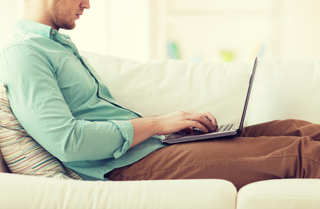 technology, home and lifestyle concept - close up of man working with laptop computer and sitting on sofa at home