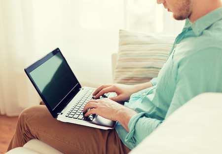 technology, leisure, advertisement and lifestyle concept - close up of man working with laptop computer and sitting on sofa at homeの写真素材