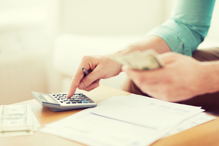 savings, finances, economy and home concept - close up of man with calculator counting money and making notes at homeの写真素材