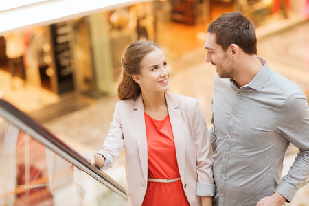 sale, consumerism and people concept - happy young couple with shopping bags rising on escalator and pointing finger in mallの写真素材