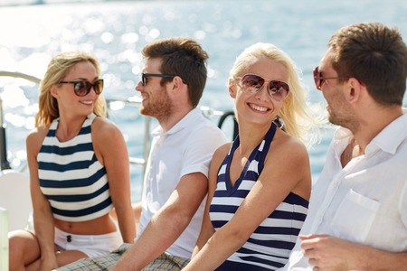 vacation, travel, sea, friendship and people concept - smiling friends sitting and talking on yacht deckの写真素材