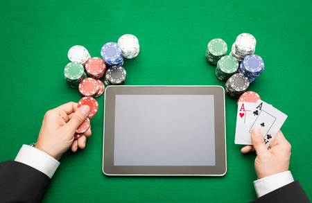 casino, online gambling, technology and people concept - close up of poker player with playing cards, tablet pc computer and chips at green casino tableの写真素材