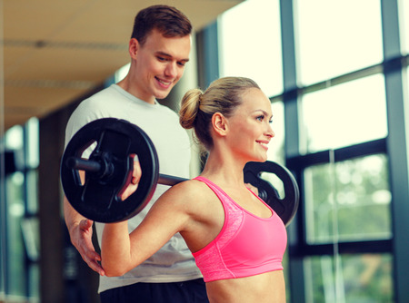 sport, fitness, lifestyle and people concept - smiling man and woman with barbell exercising in gymの写真素材