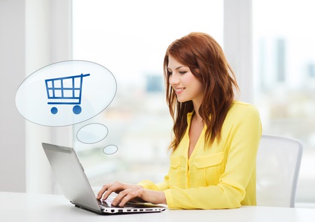 people, leisure and technology concept - smiling young woman with laptop computer and trolley icon shopping online at homeの写真素材