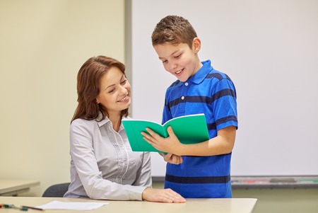 education, elementary school, learning, examination and people concept - school boy with notebook and teacher in classroomの写真素材