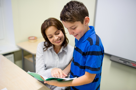 education, elementary school, learning, examination and people concept - school boy with notebook and teacher in classroomの写真素材