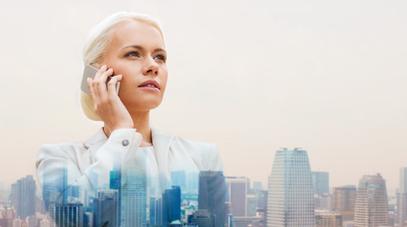 business, technology, communication and people concept - serious businesswoman with smartphone talking over city backgroundの写真素材