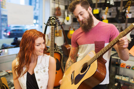 music, sale, people, musical instruments and entertainment concept - happy couple of musicians with guitar at music storeの写真素材