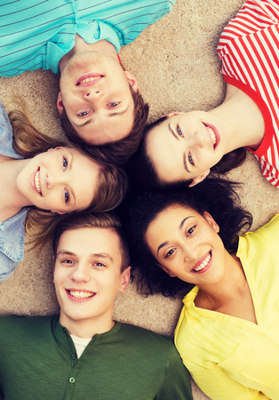 education and happiness concept - group of young smiling people lying down on floor in circleの写真素材