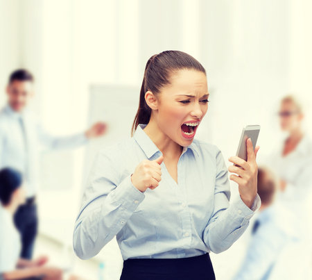 business, technology and education concept - screaming businesswoman with smartphone in officeの写真素材