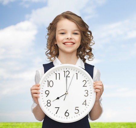 people, time management and children concept - smiling girl holding big clock showing 8 o'clock