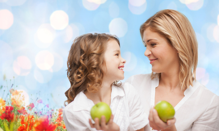 people, family, healthy eating and parenting concept - happy mother and daughter with green apples over poppy field backgroundの写真素材