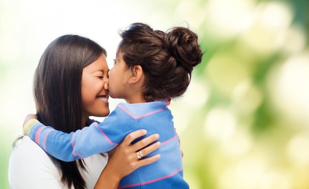 family, children and happy people concept - happy little girl hugging and kissing her mother over green backgroundの写真素材