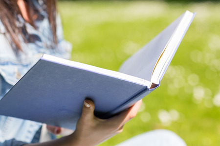 lifestyle, summer vacation, education, literature and people concept - close up of young girl reading book and sitting on grass in parkの写真素材