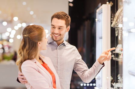 sale, consumerism and people concept - happy couple pointing finger to shopping window at jewelry store in mallの写真素材