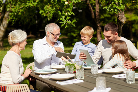 family, generation, technology, home and people concept - happy family with tablet pc computers sitting at table in summer gardenの写真素材