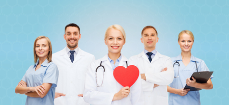 medicine, profession, teamwork and healthcare concept - group of smiling medics or doctors holding red paper heart shape, clipboard and stethoscopes over blue backgroundの写真素材