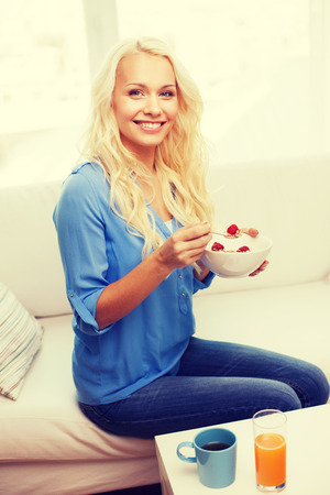 healthcare, food, home and happiness concept - smiling woman with bowl of muesli having breakfast at homeの写真素材