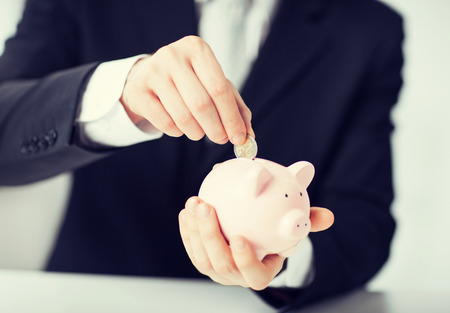 picture of man putting coin into small piggy bankの写真素材