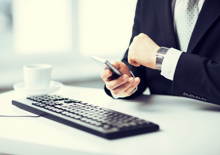 man hands with keyboard watching time and holding smartphone