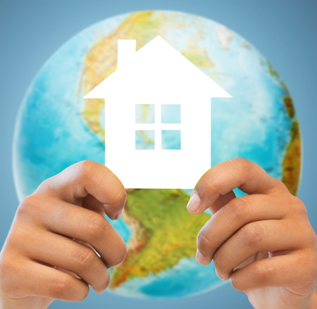 people, home, ecology and land resources saving concept - closeup of woman and man hands holding green paper house over earth globe and blue backgroundの写真素材