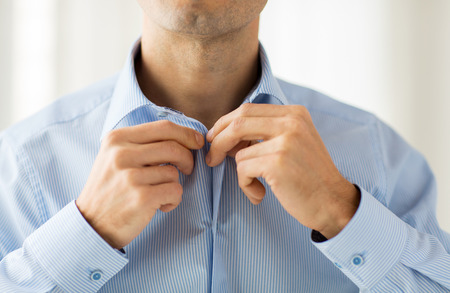 people, business, fashion and clothing concept - close up of man dressing up and fastening buttons on shirt at homeの写真素材