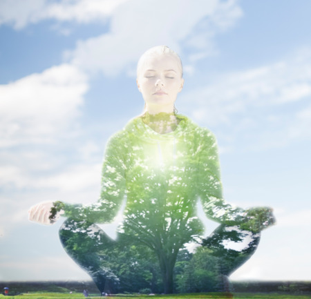 sport, fitness, yoga, double exposure and people concept - happy young woman meditating in lotus pose over blue sky and green tree backgroundの写真素材