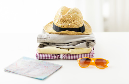 travel, summer vacation, tourism and objects concept - close up of folded clothes and touristic map...