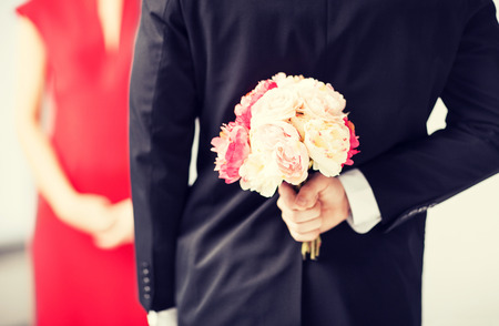 man hiding bouquet of flowers behind his back.の写真素材