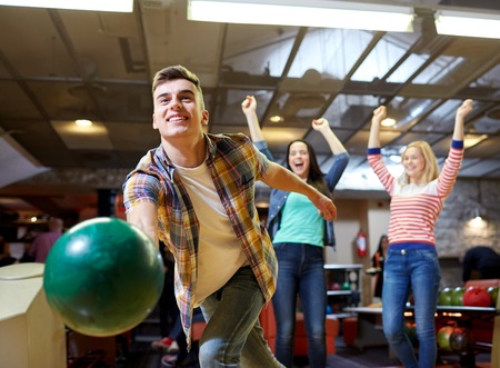 people, leisure, sport and entertainment concept - happy young man throwing ball in bowling club