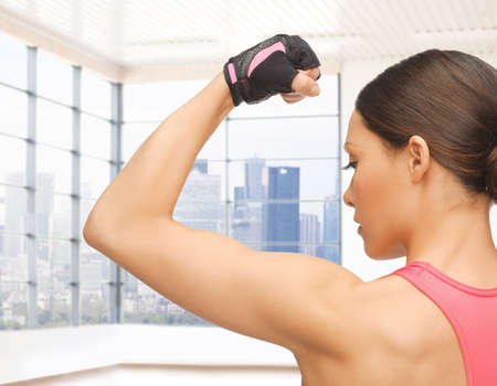 people, fitness, sport and bodybuilding concept - close up of sporty young woman flexing her biceps...