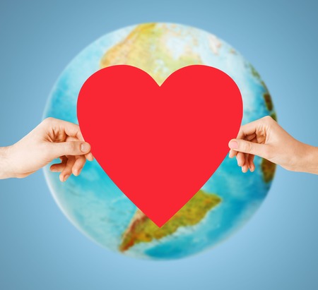 people, love, health, environment and charity concept - close up of woman hands holding red heart over earth globe and blue backgroundの写真素材