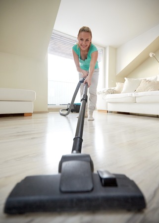 people, housework and housekeeping concept - happy woman with vacuum cleaner at homeの写真素材
