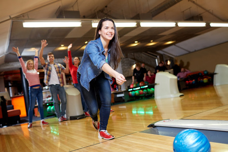 people, leisure, sport and entertainment concept - happy young woman throwing ball in bowling clubの写真素材