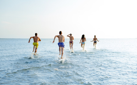 group of smiling friends in swimwear running on beach from backの写真素材