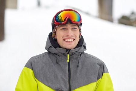 winter, leisure, sport and people concept - happy young man in ski goggles outdoorsの写真素材