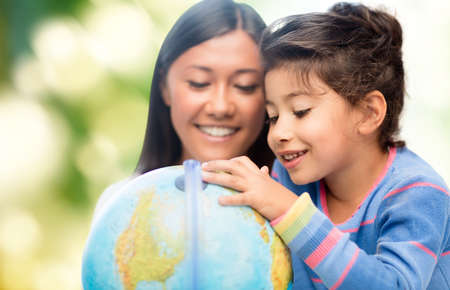 family, children, travel, geography and happy people concept - mother and daughter with globe over green backgroundの写真素材