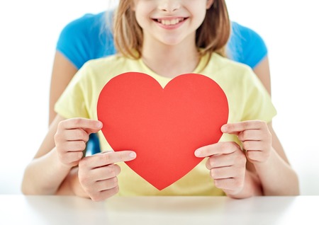 people, love, charity and family concept - close up of happy girl and mother holding red heart shape at homeの写真素材